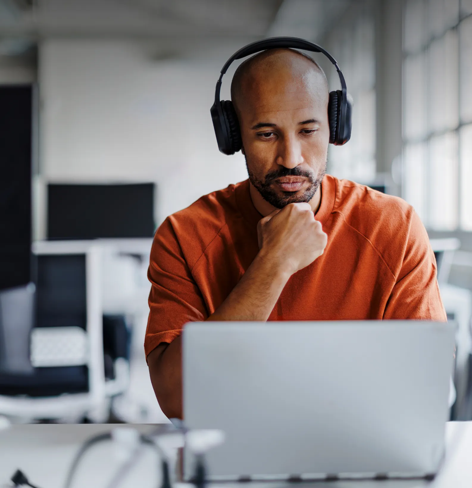 A man in headphones using his laptop and realizing that NordProtect offers more cybersecurity features than LifeLock.